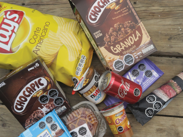 Various products with black octagonal symbols warning against high amounts of sugar, salt, calories or saturated fatty acids lie on a bench.