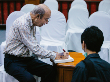 Mechai Viravaidya, aka "Mr. Condom," signs a copy of his biography, From Condoms to Cabbages, for a visitor from the International Conference on Family Planning at the Cabbages and Condoms restaurant in Pattaya, Thailand.