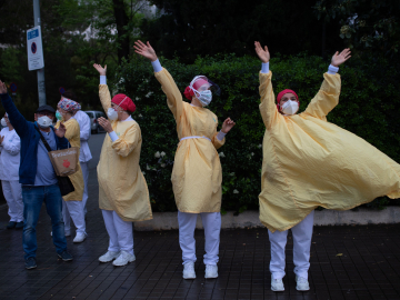 Several health care workers wearing face masks and yellow protective suits acknowledge applause outside the Hospital de Barcelona on April 13, 2020 in Barcelona, during a national lockdown to prevent the spread of the COVID-19 disease.