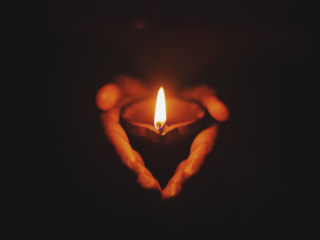 Two hands holding a lit candle.