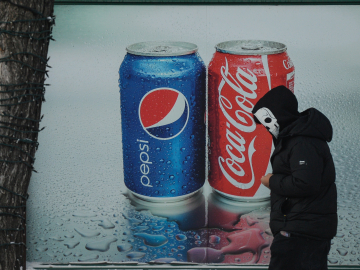 A man wearing a skull face mask walks past a Pepsi and Coca-Cola ad in the center of Edmonton, Alberta, Canada. December 30, 2021.