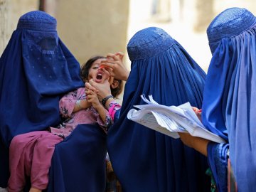 Afghan burqa-clad women health workers administer polio vaccine drops to a child during a campaign in Jalalabad on August 21, 2023.