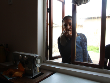 A psychologist with Living with Dignity in Tajikistan looking into an open window into a room with a sewing machine on a table.