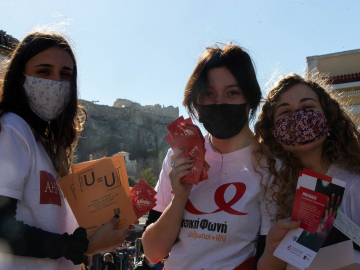 Three female volunteers, wearing cloth face masks, pose with leaflets about sexual health in Athens, Greece, on World AIDS Day, Dec. 1, 2021.