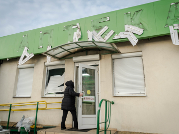 A woman enters a pharmacy after a Russian drone attack on January 31, 2024 in Kharkiv, Ukraine; the letters on the sign (anteka, which means pharmacy in Ukraine) are damaged and falling off the building front.