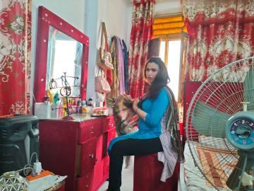 Photo of a transgender person in Pakistan, seated at a vanity with a fan in the foreground.
