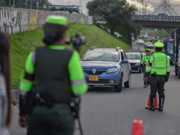 Police in Bogota wearing bright neon green safety shirts conduct speeding checks on a heavily trafficked road.