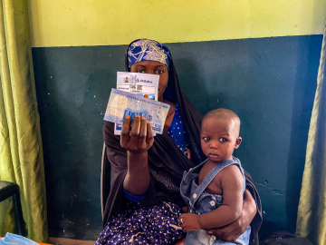 A mother holds up the cash incentive she received at the Farfaru clinic upon vaccinating her child.