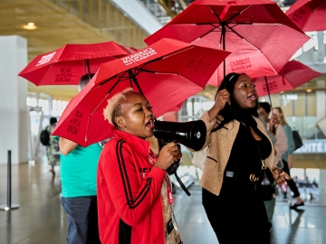 Women with red umbrellas that say &quot;Sex Work is Work&quot; raise awareness at ICFP 2025.