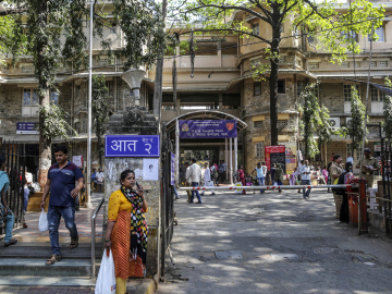 A woman uses her mobile phone at an entrance to the three-story gray stone and yellow King Edward Memorial (KEM) Hospital in the Parel area of Mumbai, India.