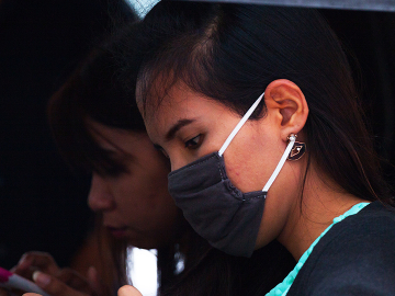 Young Thai girl with mobile and surgical mask.