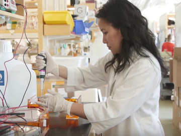 Woman working in laboratory. Still from MalariaX Trailer