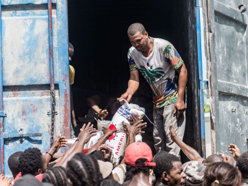 A man gives a bag of rice to a crowd of earthquake victims gathered for the distribution of food and water at the &quot;4 Chemins&quot; crossroads in Les Cayes, Haiti on August 20, 2021.