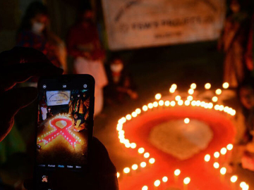 A volunteer takes pictures with her mobile phone of others lighting candles in the shape of a red ribbon during an awareness event on the eve of World AIDS Day in Siliguri, West Bengal, India, on November 30, 2021.