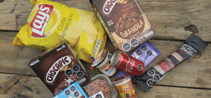 Various products with black octagonal symbols warning against high amounts of sugar, salt, calories or saturated fatty acids lie on a bench. 