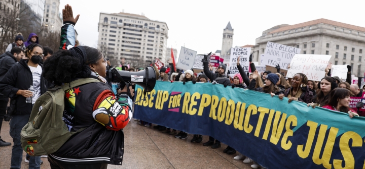 A woman speaks into a microphone, addressing a crowd behind a banner reading "Rise up for Reproductive Justice" at a January 22 protest in Washington, DC. 