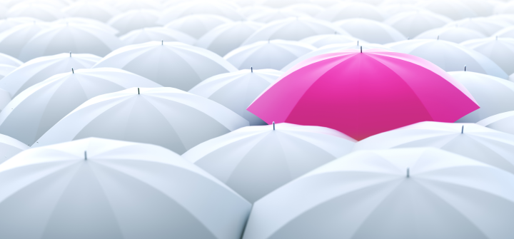 A pink umbrella stands out among many white umbrellas.
