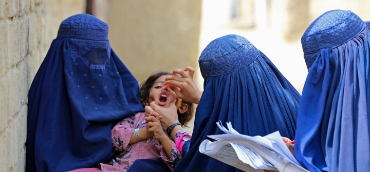 Afghan burqa-clad women health workers administer polio vaccine drops to a child during a campaign in Jalalabad on August 21, 2023.