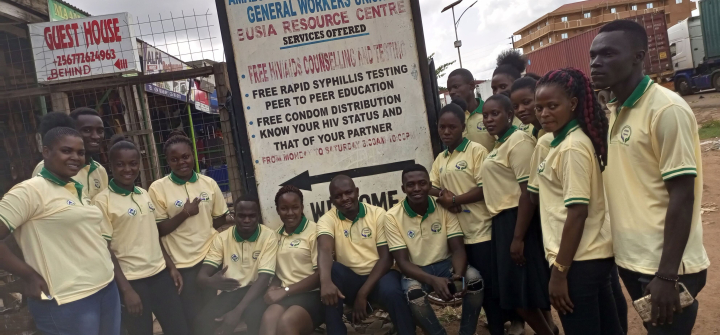 Staff at ATGWU wear yellow polo shirts standing in front of a sign describing the facility's services