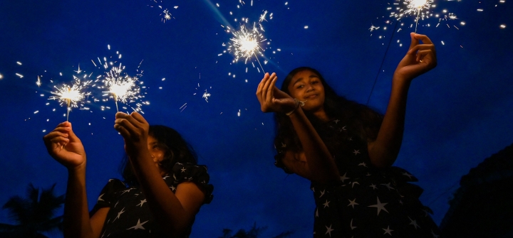 Two girls light sparklers against a blue sky background during the Sinhala and Tamil New Year celebrations in Pugoda on April 14, 2023. 