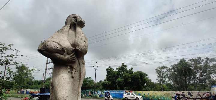 A statue of a mother holding her child with her hand over her face, against a cloudy grey sky. 