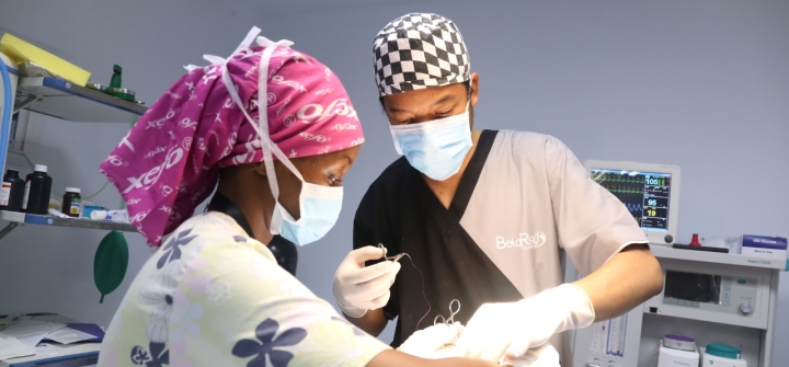 Belinda Karimi, wearing a surgical mask and a hot pink head covering, performs surgery with a colleague.