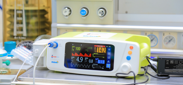 Image of a capnograph surgical monitoring device, a small whie box with a screen displaying vital statistics.