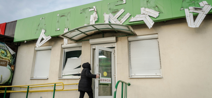 A woman enters a pharmacy after a Russian drone attack on January 31, 2024 in Kharkiv, Ukraine; the letters on the sign (anteka, which means pharmacy in Ukraine) are damaged and falling off the building front.