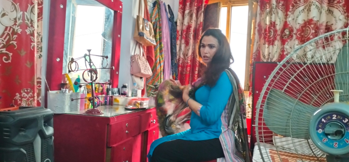 Photo of a transgender person in Pakistan, seated at a vanity with a fan in the foreground.