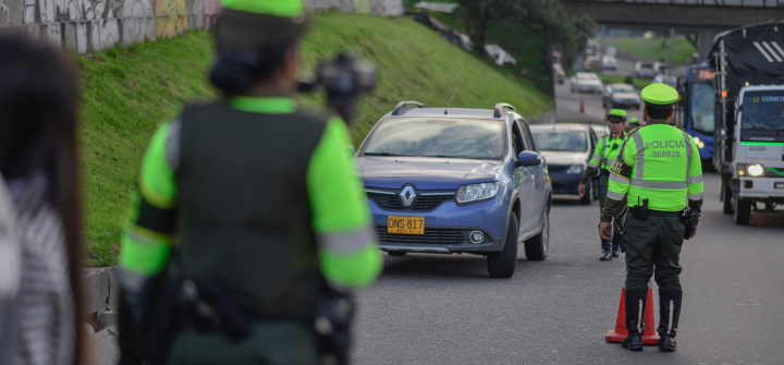 Police in Bogota wearing bright neon green safety shirts conduct speeding checks on a heavily trafficked road.