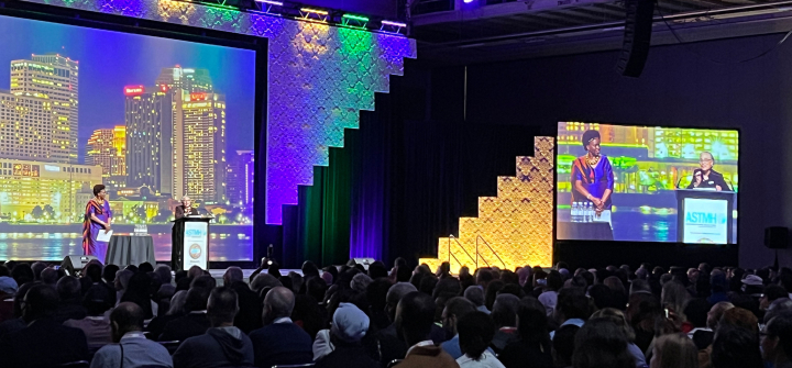 Monique Wasunna stands on a stage delivering her keynote to a packed audience. 