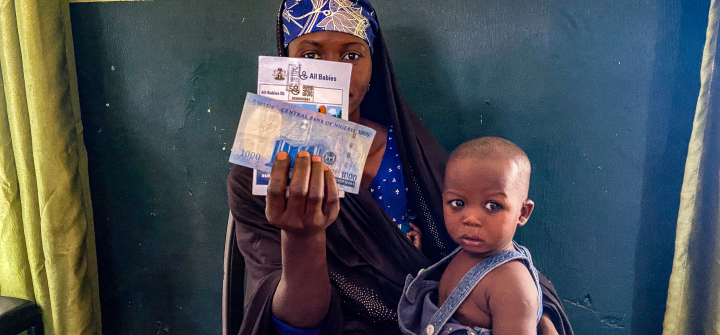 A mother holds up the cash incentive she received at the Farfaru clinic upon vaccinating her child. 