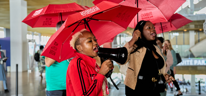 Women with red umbrellas that say "Sex Work is Work" raise awareness at ICFP 2025.