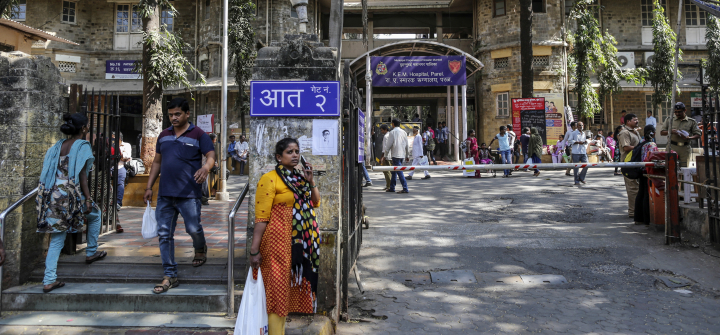 A woman uses her mobile phone at an entrance to the three-story gray stone and yellow King Edward Memorial (KEM) Hospital in the Parel area of Mumbai, India.
