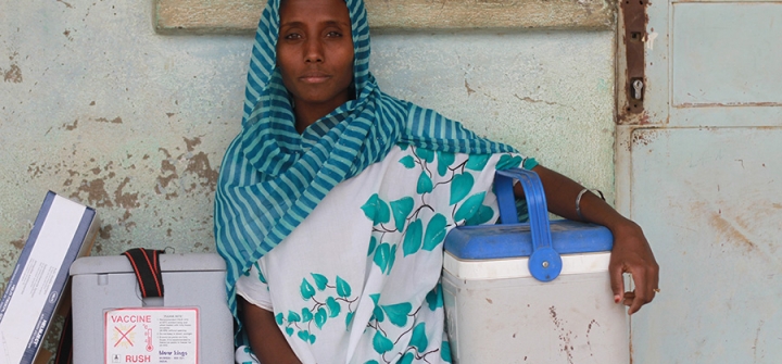 A woman, Sity Mohamed, HEW, outside her Health Post in Yalo, Ethiopia, sitting with a box of syringes and two cold boxes. 