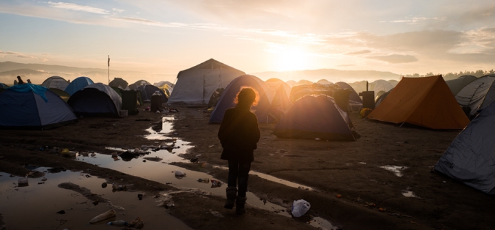 A young refugee in front of hundreds of tents, during sunrise in a refugee camp in Idomeni, Greece in March 2016. 
