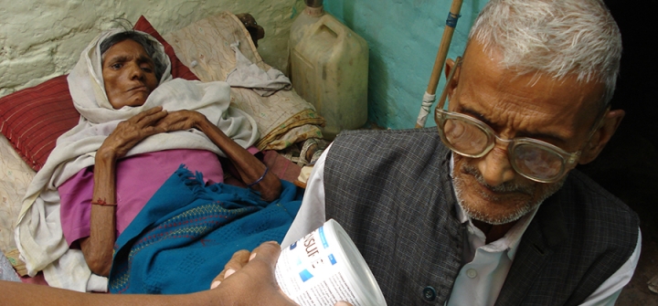A home care nurse (not seen) in New Delhi, India, offers a tin of nutritional supplement to the husband of a patient with cancer of the salivary gland in the terminal stages. 
