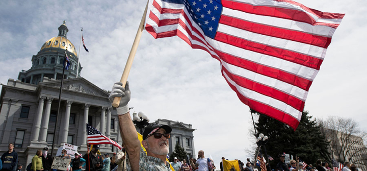 A man waves a US flag in front of the Colorado State Capitol building during a demonstration to protest coronavirus stay-at-home orders.  Denver, April 19, 2020. Image: Jason Connolly/AFP/Getty 