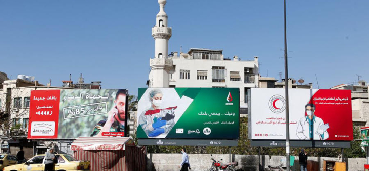 A Syrian man wearing a face mask walks in front of COVID-19 posters, Damascus. April 1, 2020.