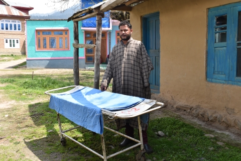 Zahoor Ahmed Bhat stands outside his house in the Anantnag district of South Kashmir with the stretcher that his wife, Shakeela AkhterAkhter died on before she could get to an emergency maternal health care center. Image by Aliya Bashir.
