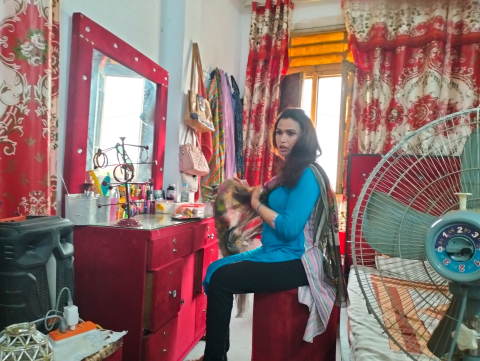 Photo of a transgender person in Pakistan, seated at a vanity with a fan in the foreground.