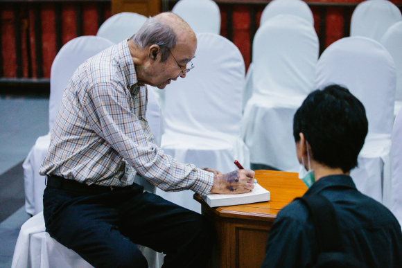 Mechai Viravaidya, aka "Mr. Condom," signs a copy of his biography, From Condoms to Cabbages, for a visitor from the International Conference on Family Planning at the Cabbages and Condoms restaurant in Pattaya, Thailand. 