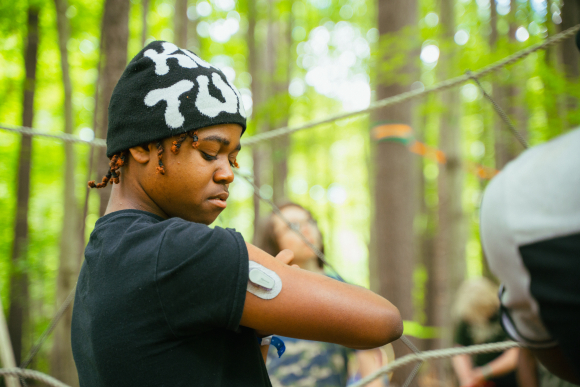 A camper at Camp Ho Mita Koda wearing a black hat and black t-shirt shows an insulin patch on their arm.