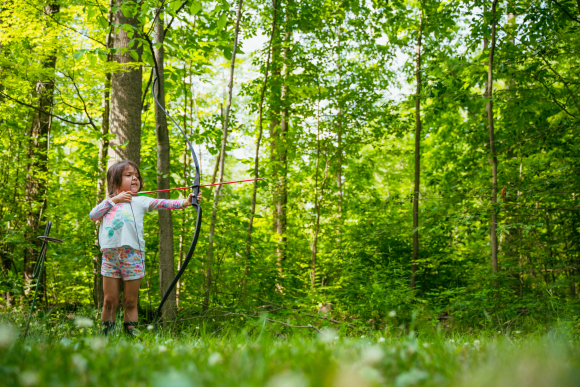 A young camper holds a bow and arrow, poised for release, at Courtesy of Camp Ho Mita Koda