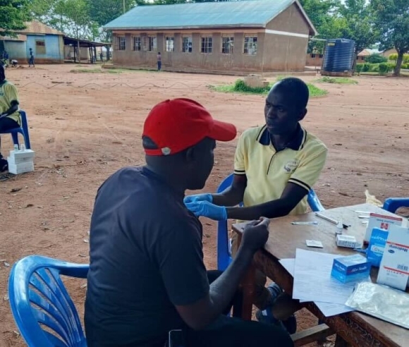 A health worker administers a test to a client seated at an outdoor table.