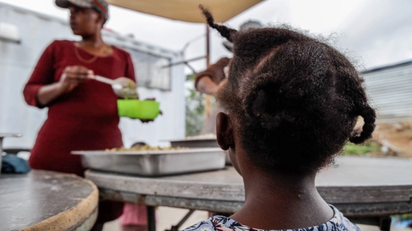 Child waiting for food being served by soup kitchen volunteers.