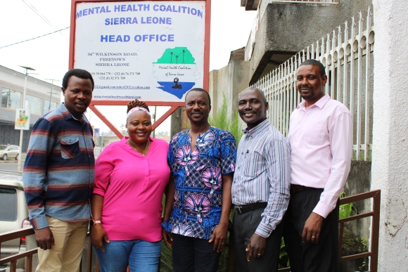 Photo of the five founders of the Mental Health Coalition in front of the head office sign.