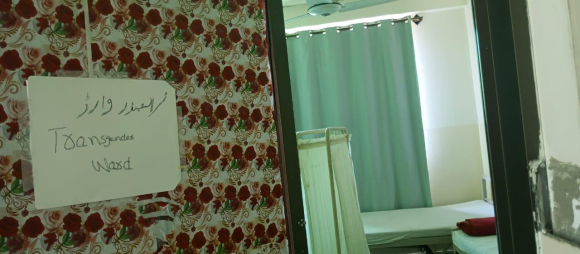 A photo shows the entrance to a hospital room, with divider curtains, and a sign on a floral screen that says "Transgender ward" in Urdu and English.