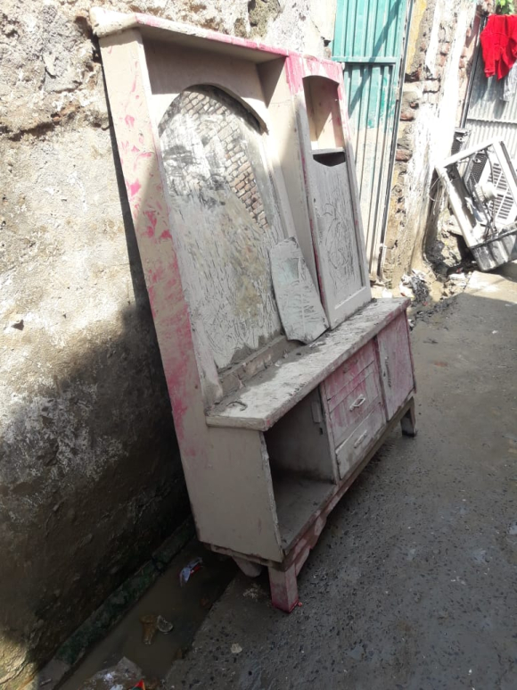 An old dressing table with white and pink chipped paint and other household items belonging to a group of transgender people are kept outside a home in Nowshera district, shown on a sunny day.