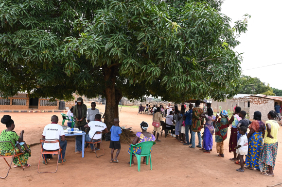 People queue for sleeping sickness screening in Paanenefla village, Ivory Coast, under the canopy of a green tree.